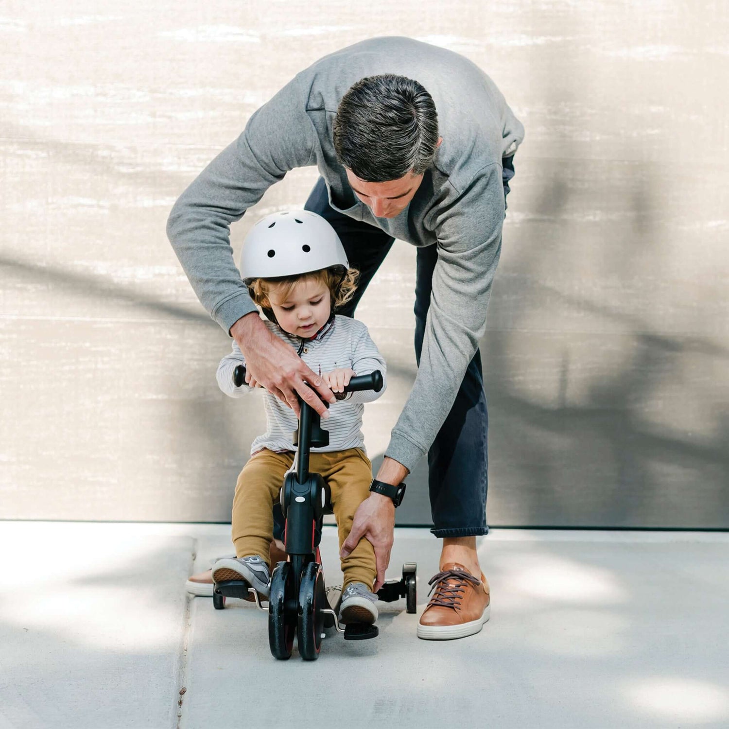 dad helping toddler use pedals on red Larktale Scoobi in tricycle mode