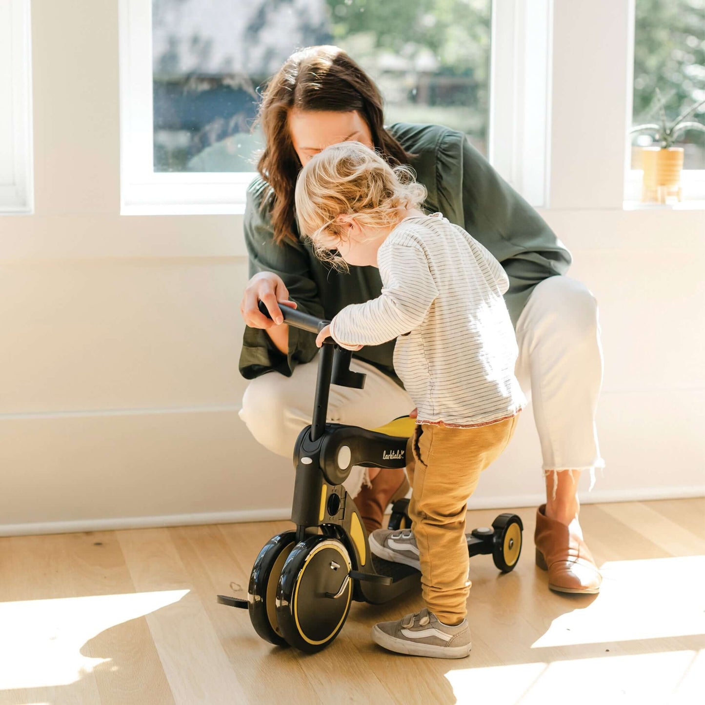 mother helping toddler ride yellow larktale scoobi in tricycle mode