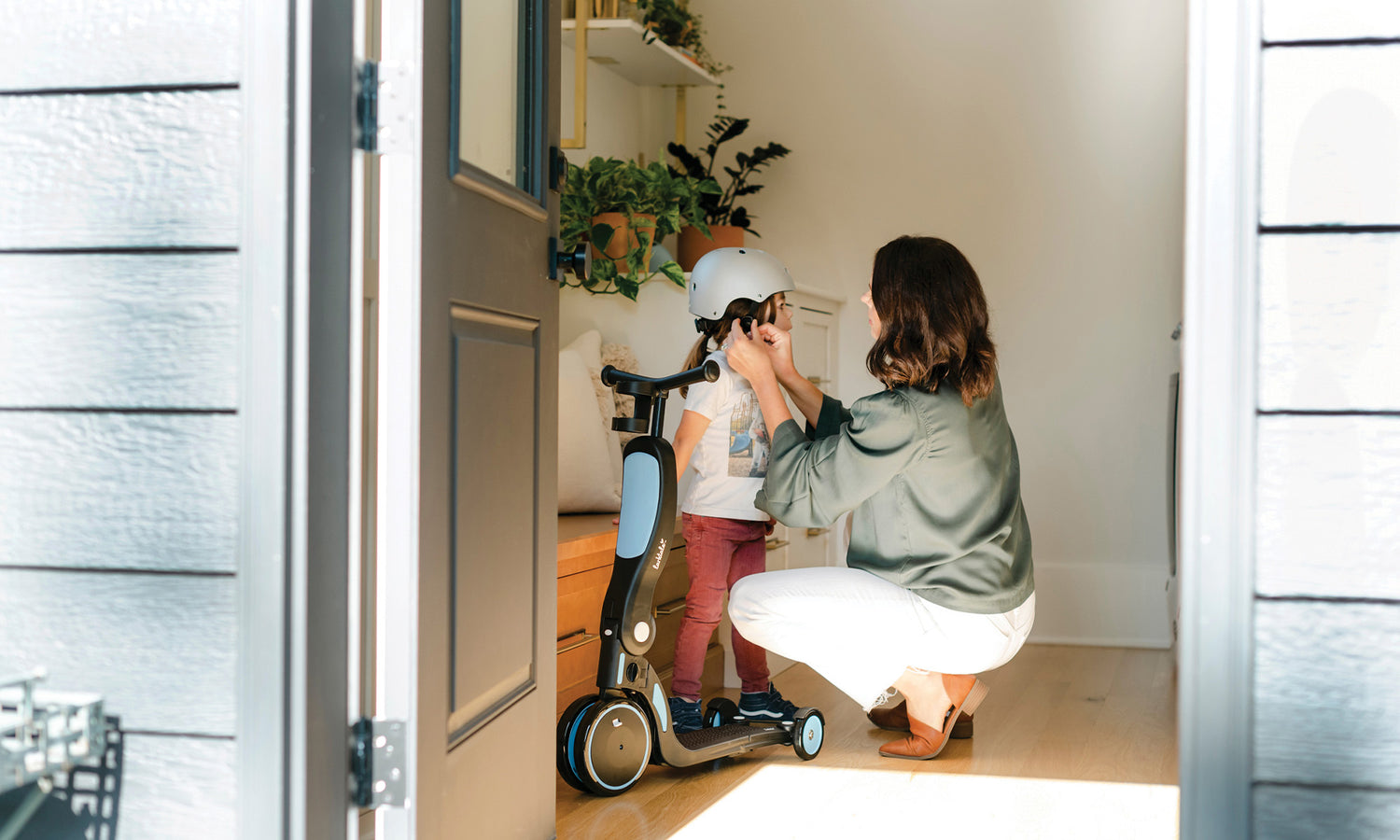 mother putting helmet on three year old child who is getting ready to ride scooter