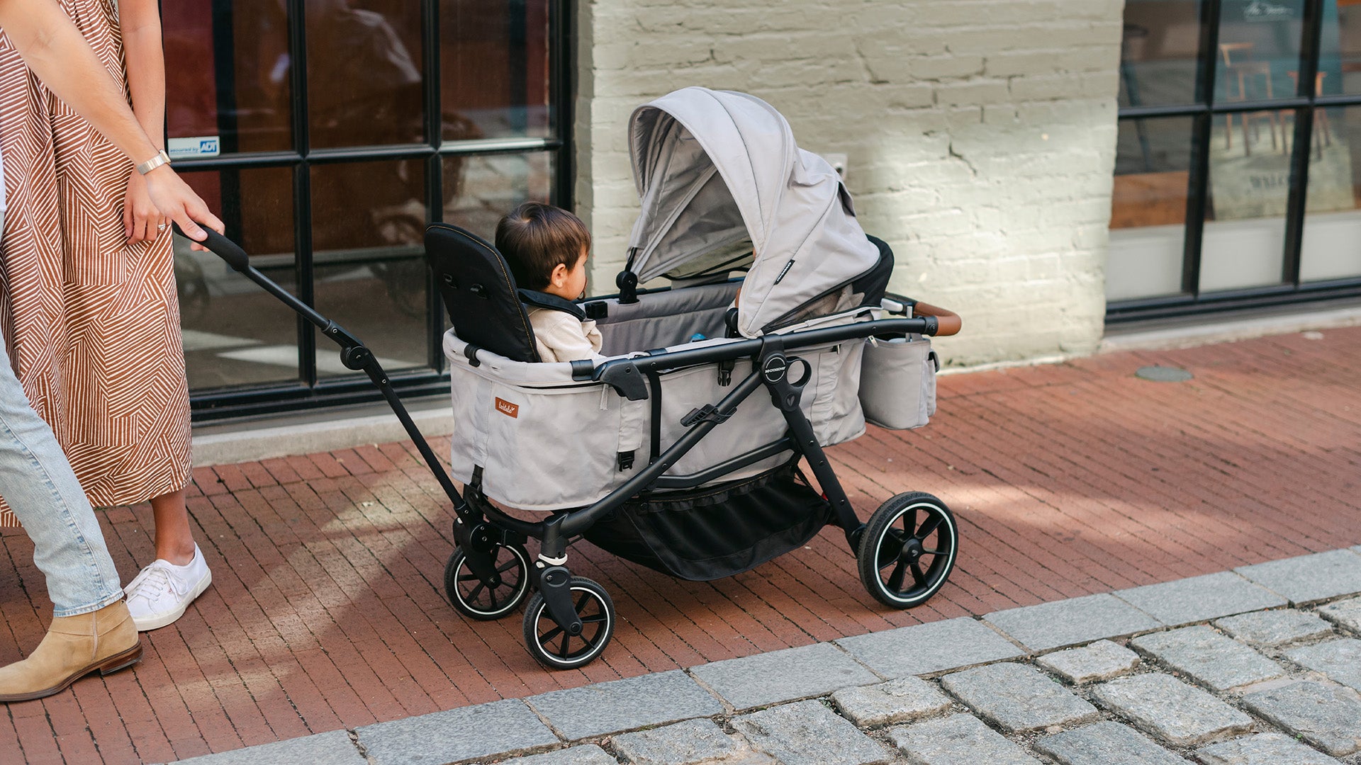 father pulling two children in grey wagon stroller